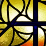 A stained-glass window depicting a Presbyterian cross with an American flag in the background. - American Presbyterian Church